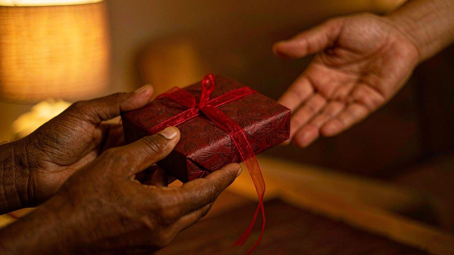 A small gift wrapped in red paper being offered with both hands
