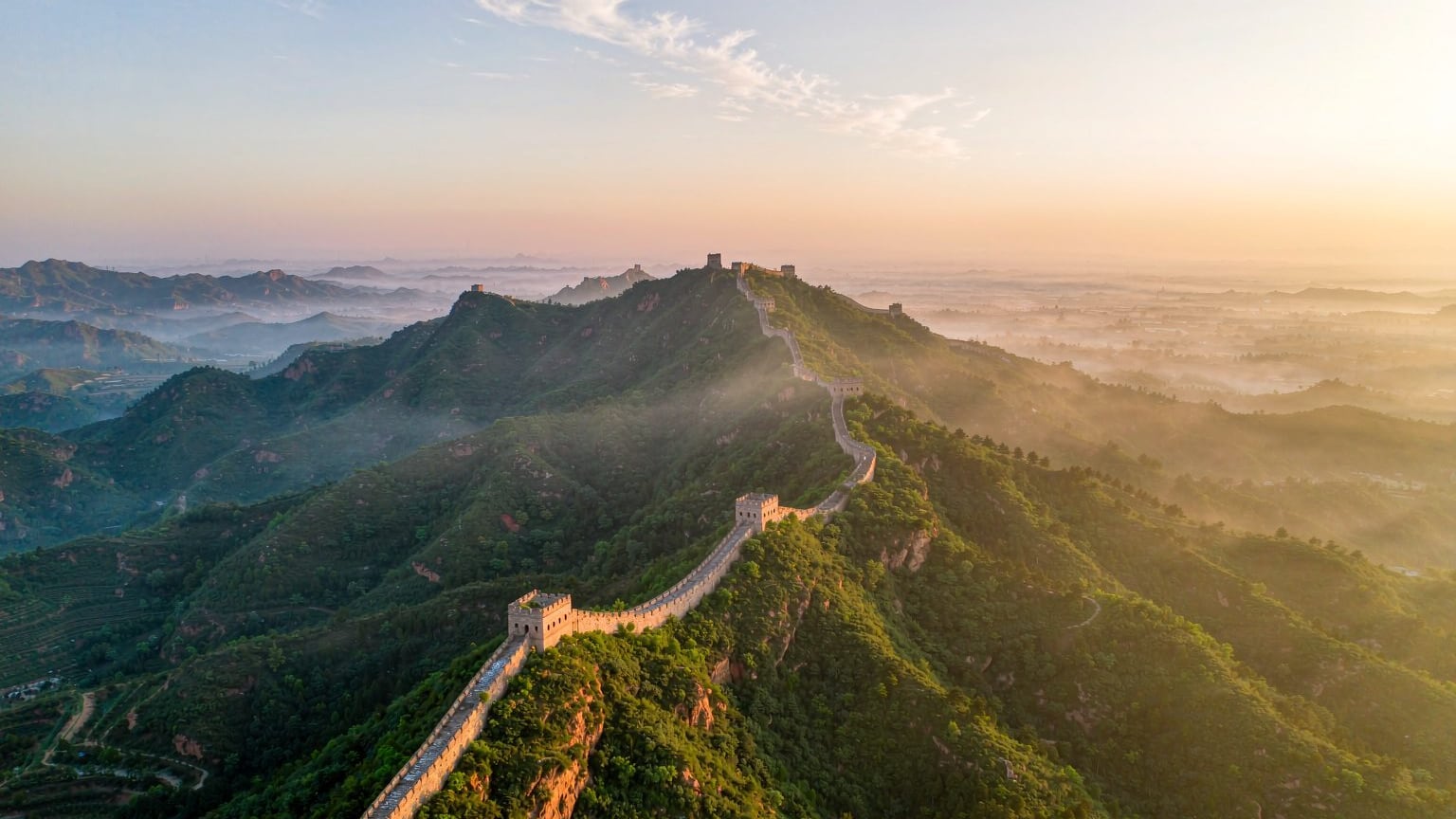 The Great Wall of China winding over green mountains at sunrise