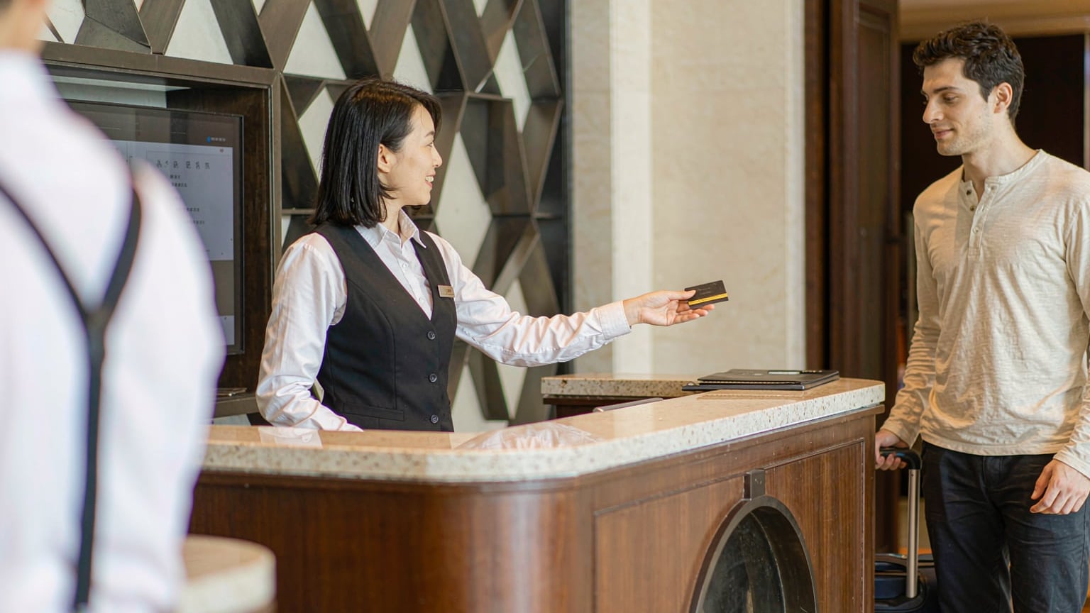 A hotel receptionist handing a key card to a foreign guest at a modern hotel front desk in China